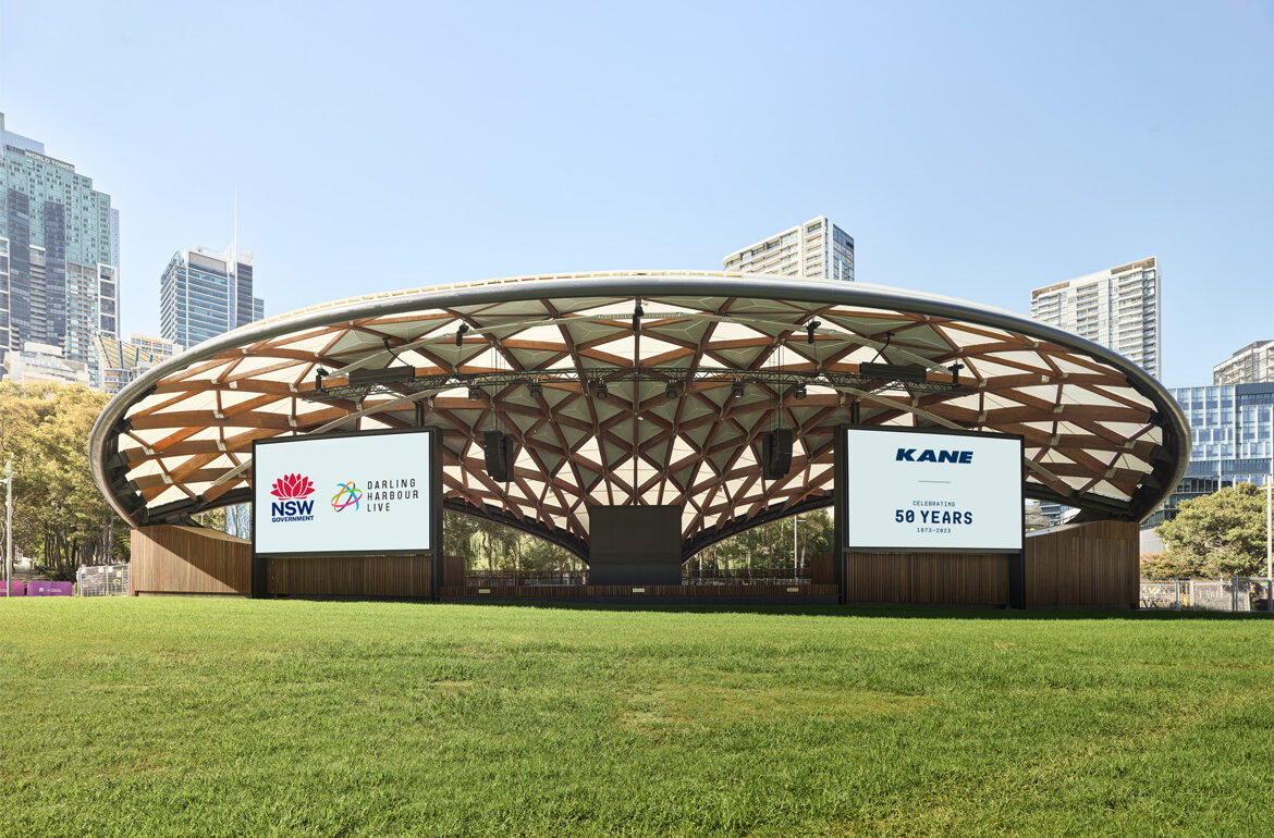 The completed Tumbalong Green Stage: an elliptical timber-and-steel gridshell canopy over an outdoor stage in Darling Harbour, Sydney.